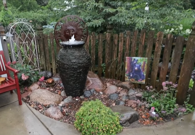 Stacked-stone urn fountain with a sun sculpture in a river-rock garden bed