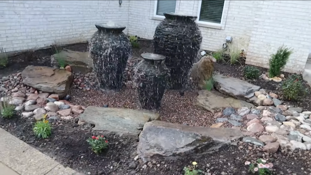 Three overflowing urn fountains of different heights set in gravel beside a home