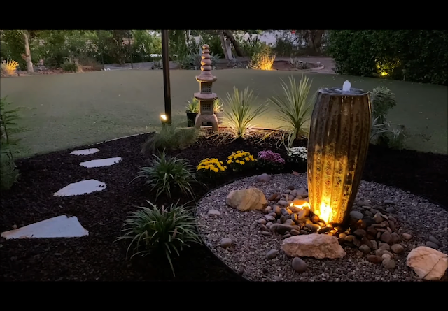 Uplit ceramic urn fountain at dusk with stepping stones and a stone lantern