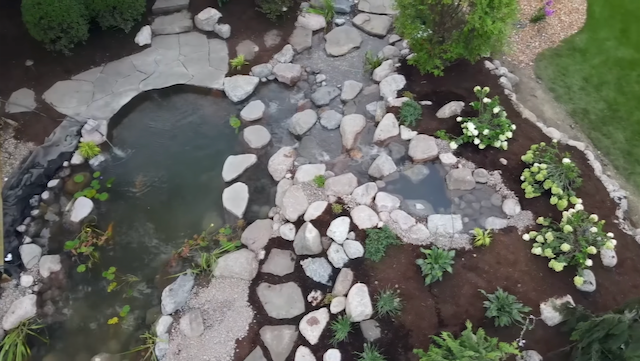 Aerial view of a pond, rocky stream, and flagstone path through mulched plantings