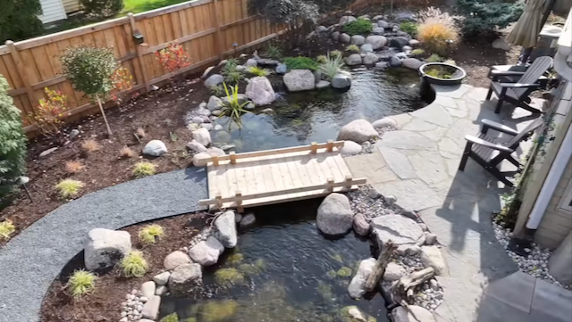Wooden footbridge crossing a backyard stream beside a flagstone patio