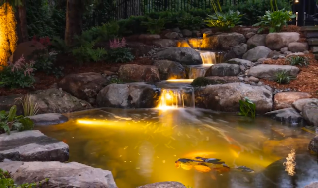 Warm underwater lighting on a multi-tier waterfall and koi pond at dusk