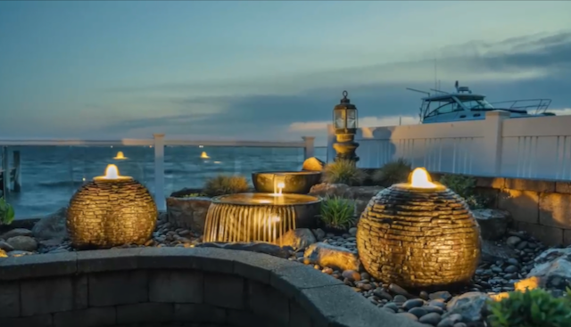 Illuminated spherical and overflowing fountains at twilight on a waterfront patio