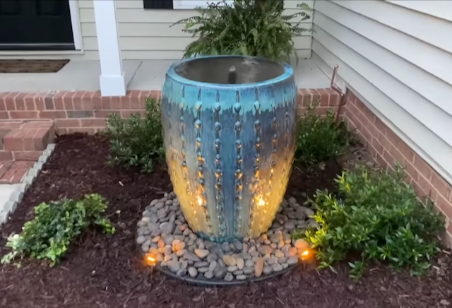 Teal and amber glazed urn fountain glowing at the base beside a home entry