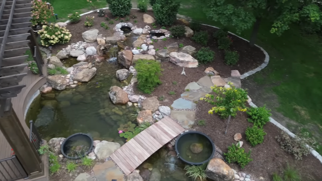 Overhead view of a boulder-lined pond, wooden plank bridge, and winding garden path